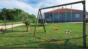 A playground with swings and a fenced area, a tree, and a house with a red roof in the background. - Holiday house Flora with pool by Interhome (Crno)