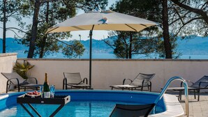 A pool area with lounge chairs, a table with drinks, and a large umbrella. - Beautiful villa Horizon by Interhome (Crno)