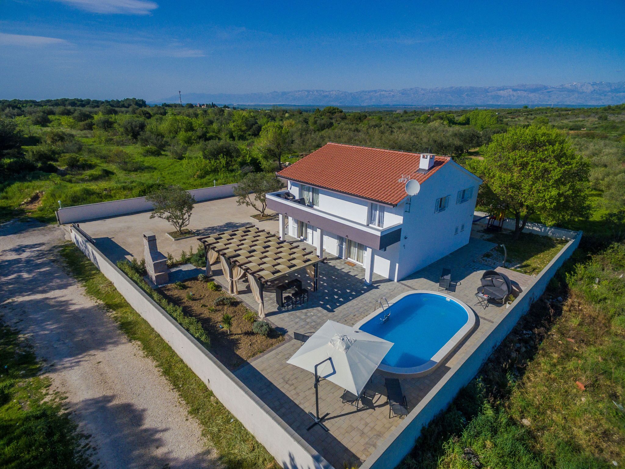 A two-story house with a swimming pool, outdoor seating, and a view of distant mountains.