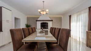 A modern dining room with a long table, brown upholstered chairs, a chandelier, and a fireplace. - Beautiful villa Horizon by Interhome (Crno)