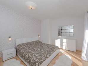 Ein Schlafzimmer mit einem gemusterten Bett, einem weißen Nachttisch, einer Kommode und einem an der Wand befestigten Spiegel.