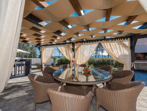 An outdoor patio with a round glass table surrounded by wicker chairs, a pool in the background, and a pergola overhead. - Beautiful villa Horizon by Interhome (Crno)