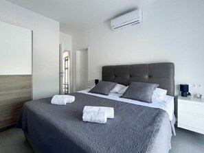 Quarto de hotel moderno com cama grande, mesa de cabeceira, ar condicionado e vista para o corredor.