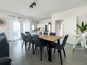 Eine moderne Küche mit weißen Schränken, einem Esstisch mit Stühlen und einem großen Fenster mit Vorhängen.