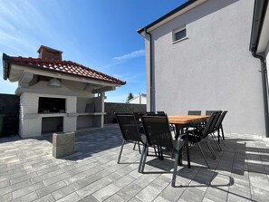 Eine Terrasse im Freien mit Backsteinboden, einem Holztisch und schwarzen Stühlen.