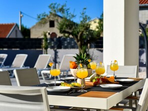 An outdoor dining area with a table set for two, featuring a fruit bowl, glasses of orange juice, and a variety of fruits. - Villa Nostro Porto with pool by Interhome (Crno)