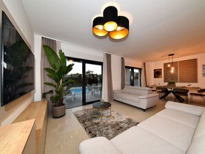 A modern living room with a sofa, a coffee table, and a TV. There is a dining area with a table and chairs. - Villa Nostro Porto with pool by Interhome (Crno)