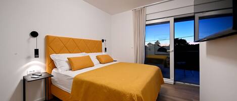 A modern hotel room with a bed, a bedside table, an air conditioning unit, and a large window with a view.
