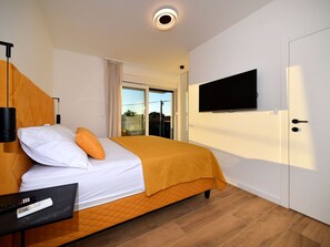 A hotel room with a bed, a flat-screen TV mounted on the wall, a laptop on the nightstand, and a window with curtains. - Villa Nostro Porto with pool by Interhome (Crno)