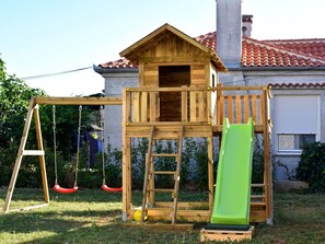 A wooden playhouse with a slide and swings, set against a house with a tiled roof. - Villa Nostro Porto with pool by Interhome (Crno)
