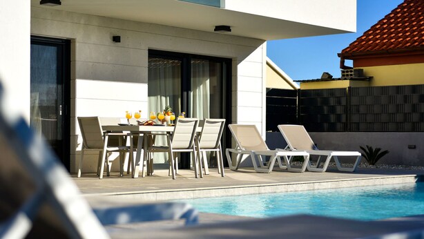 Un espace piscine extérieur moderne, doté de chaises longues et d’une table à manger où sont servis les articles pour le petit-déjeuner.