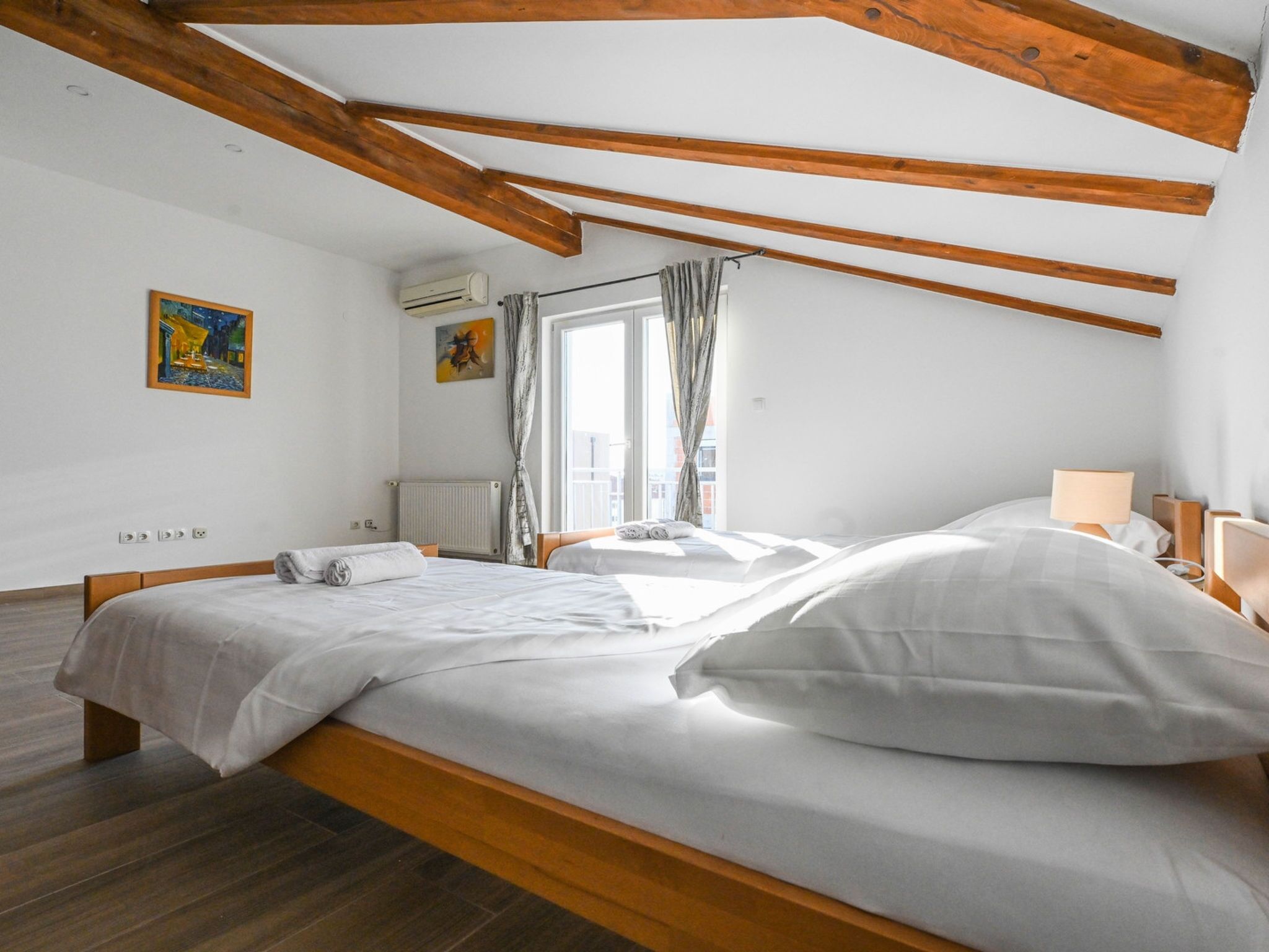 Een slaapkamer met een houten plafond, twee bedden, een raam met gordijnen en kunst aan de muur.