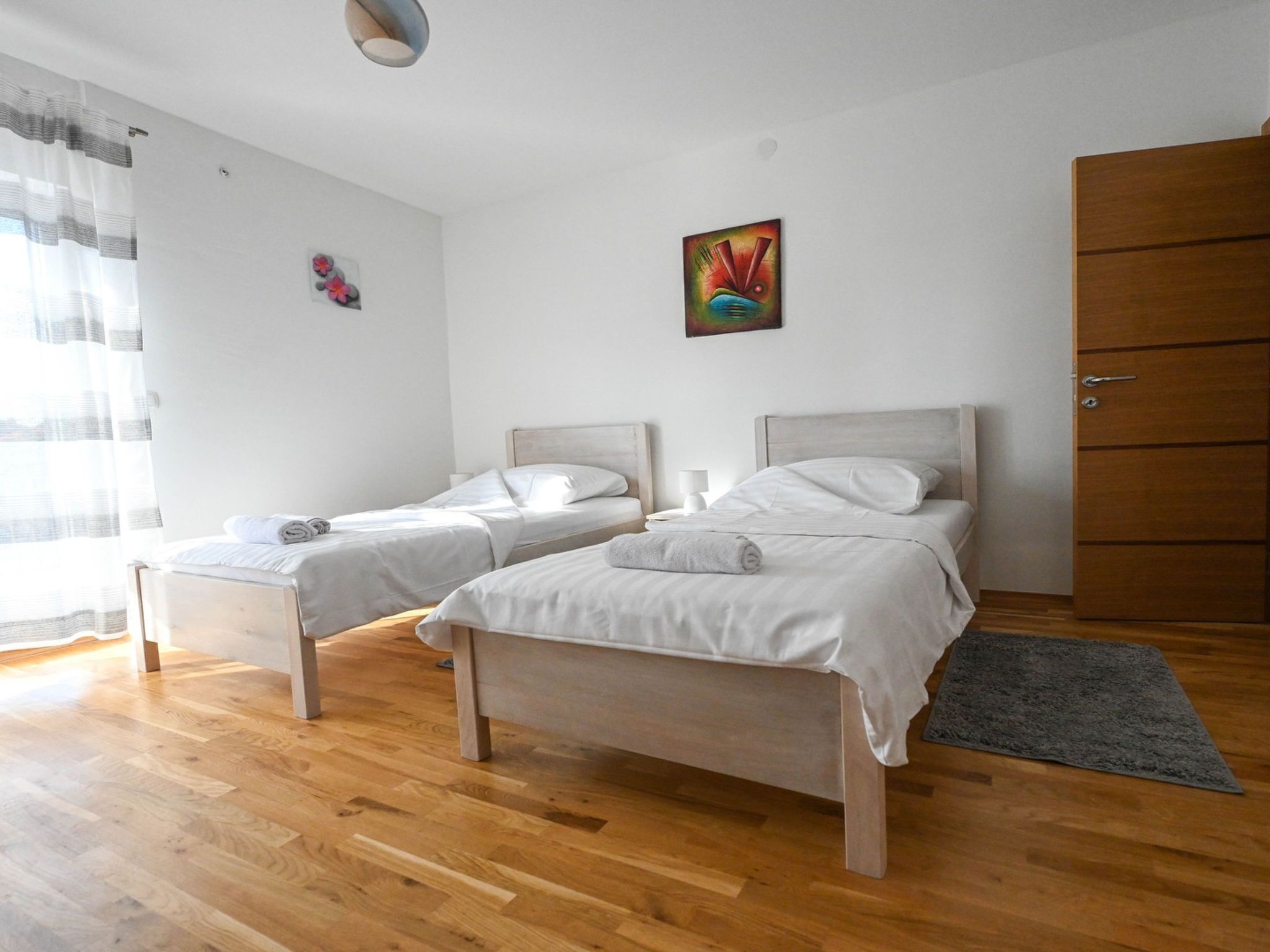 Una habitación con dos camas individuales, un armario de madera, un cuadro en la pared y una ventana con cortinas.
