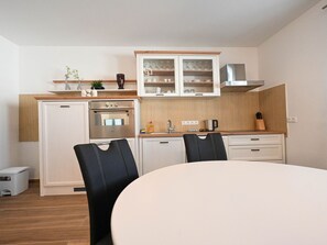 A compact kitchen with a refrigerator, oven, and cabinets, a dining table with chairs, and a small trash bin. - Holiday Home Urbana with pool by Interhome (Crno)