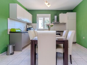 Uma cozinha moderna com armários brancos, uma mesa de jantar com cadeiras e uma janela com vista para o verde.