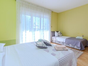 Una habitación con dos camas, un ventanal con cortinas translúcidas y suelo de madera.