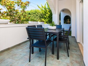 Eine Terrasse im Freien mit Tisch und Stühlen, umgeben von einer weißen Mauer und Grünpflanzen.