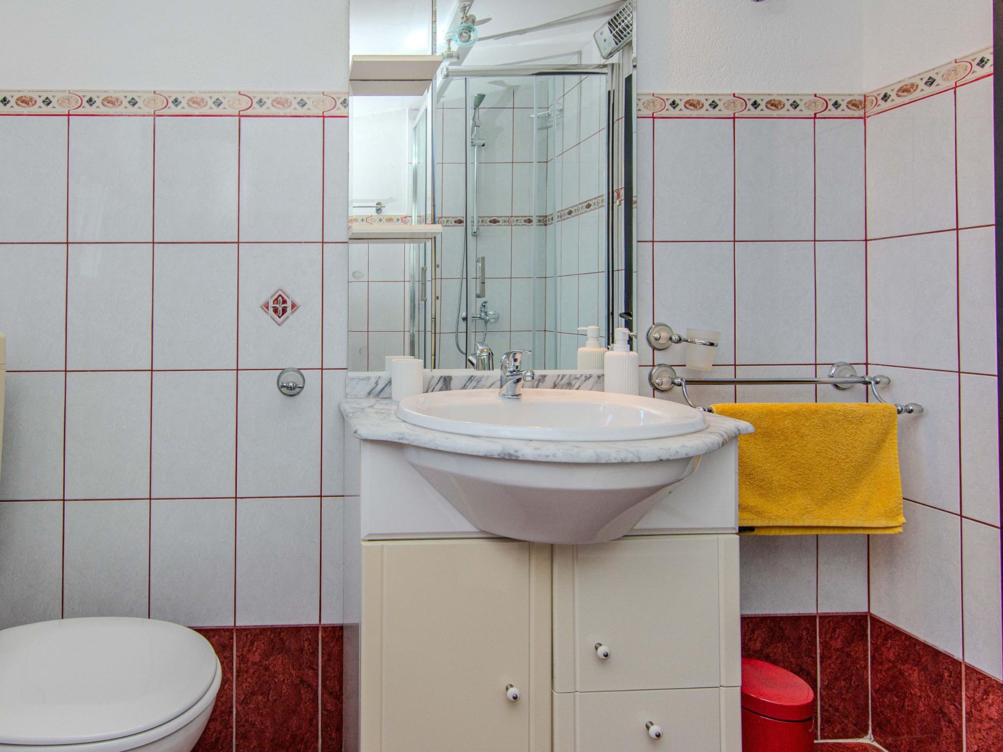 Une salle de bain avec un lavabo blanc, un miroir et des toilettes. Une serviette jaune est suspendue à un porte-serviettes.