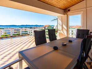 Un balcón con mesa y sillas, con vista al mar y casas.