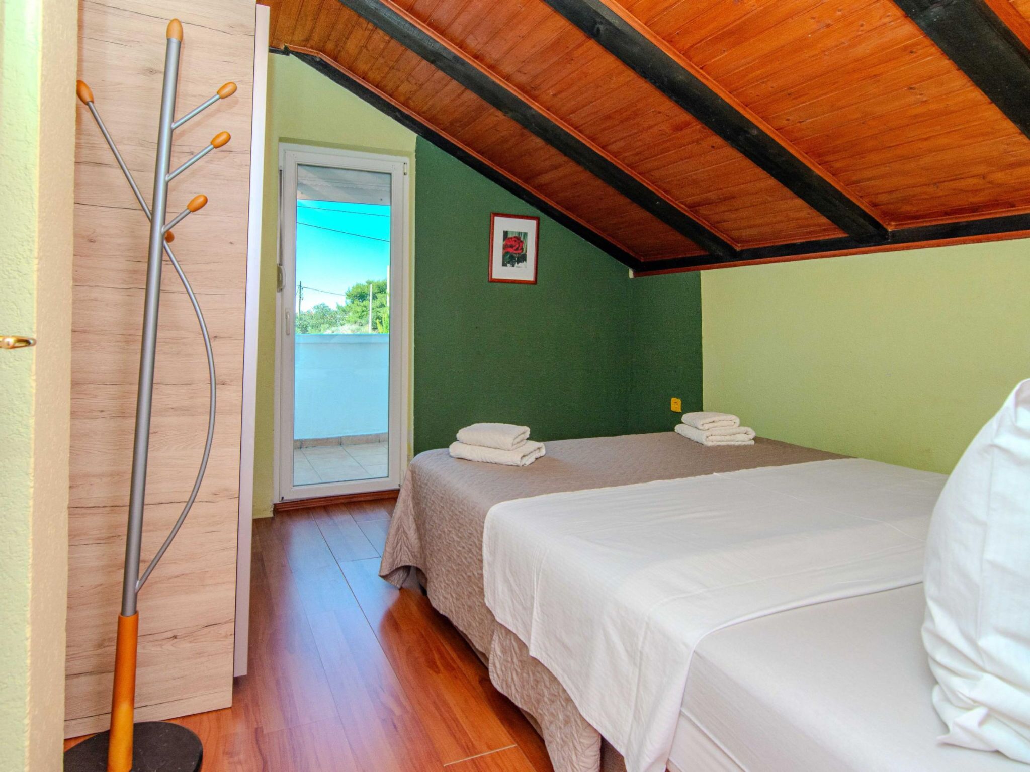 Une pièce avec deux lits, un plancher en bois, une porte donnant sur l’extérieur et un plafond avec des poutres apparentes.