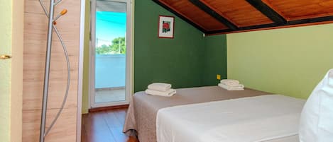 A room with two beds, a wooden floor, a door leading outside, and a ceiling with exposed beams.