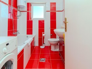 Un baño con bañera, inodoro y lavamanos, con azulejos rojos y blancos.