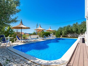 Una piscina con sillas de descanso y sombrillas, rodeada de vegetación y un cielo despejado.