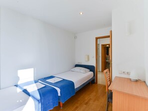 Une petite pièce lumineuse, avec un lit simple, une table en bois et une porte donnant sur une salle de bain.