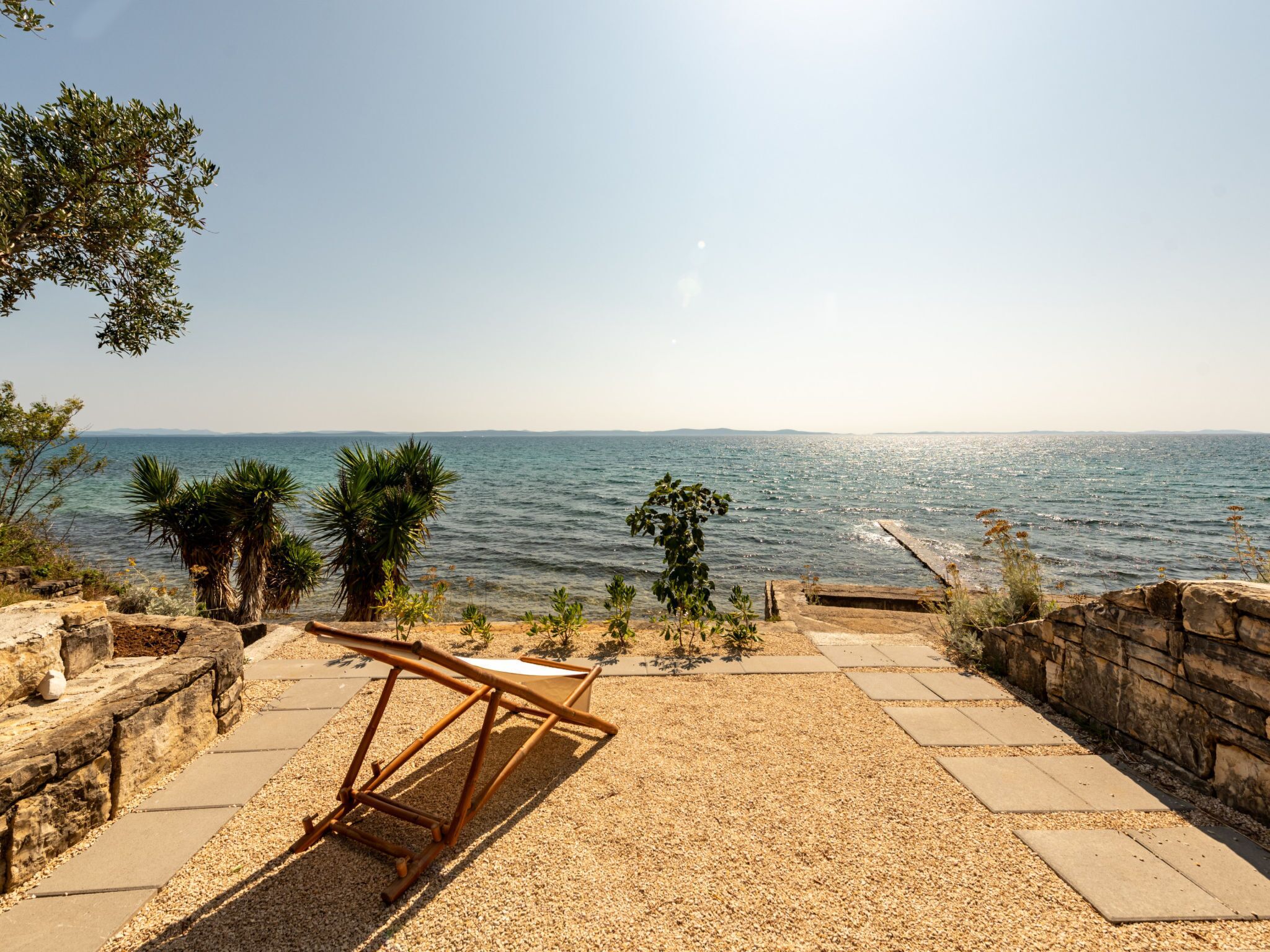 A patio with a view of the sea, a wooden chair, and a small table.