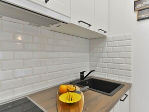 A kitchen with white subway tiles, a black sink, and a wooden countertop with a citrus juicer. - Apartment  by Interhome (Vir)