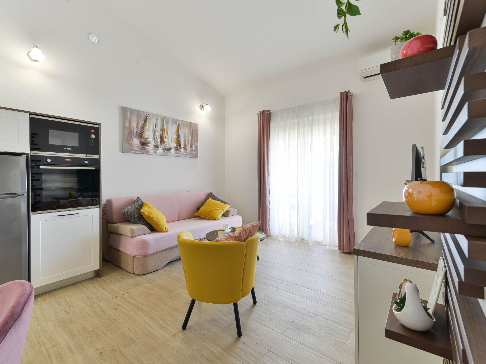 A modern living space with a kitchen, a sofa, a yellow chair, and a dining area with a shelf.