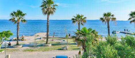 A beachside parking area with a car, palm trees, and a clear view of the sea.