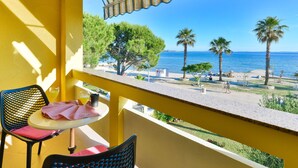 En balkon med gule vægge, et bord med en stol og udsigt til havet med palmer.