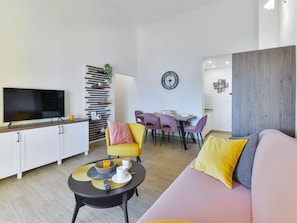 A modern living room with a sofa, coffee table, TV, and dining area with chairs and a table. - Apartment  by Interhome (Vir)
