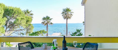 A round table with chairs, a bottle, and glasses on a balcony overlooking the sea.