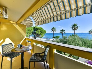 A balcony with yellow walls, a striped awning, and a view of the sea and palm trees. - Apartment  by Interhome (Vir)