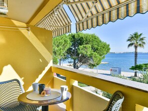 Ein Balkon mit Tisch und Stühlen, mit Blick auf einen Strand mit Bäumen und einer Palme.