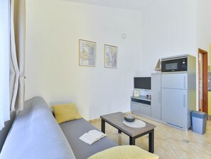 Un salon moderne avec un canapé gris, une petite table et un coin cuisine équipé d’un four à micro-ondes et d’un réfrigérateur.