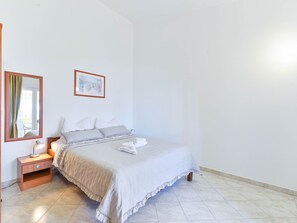 Ein Hotelzimmer mit Bett, Nachttisch, Nachttischlampe, einem gerahmten Bild an der Wand und einem Fenster mit Vorhängen.