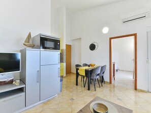 A compact kitchen with a microwave, a refrigerator, and a dining area with chairs and a table. - Apartment  by Interhome (Vir)