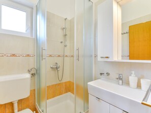 A modern bathroom with a glass-enclosed shower, a white sink, and a mirror above it. - Apartment  by Interhome (Vir)