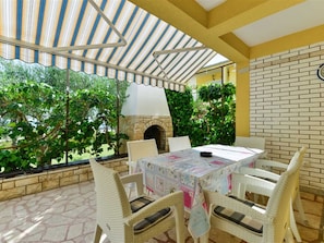 An outdoor patio with a brick wall, a stone floor, wicker furniture, and a table with a floral tablecloth. - Apartment  by Interhome (Vir)