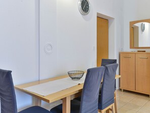 Un comedor con una mesa de madera, cuatro sillas, un reloj de pared, una puerta y un espejo sobre un mueble de madera.