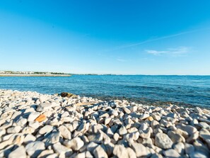 Ein Kiesstrand mit klarem, blauem Wasser und einer fernen Küstenlinie.