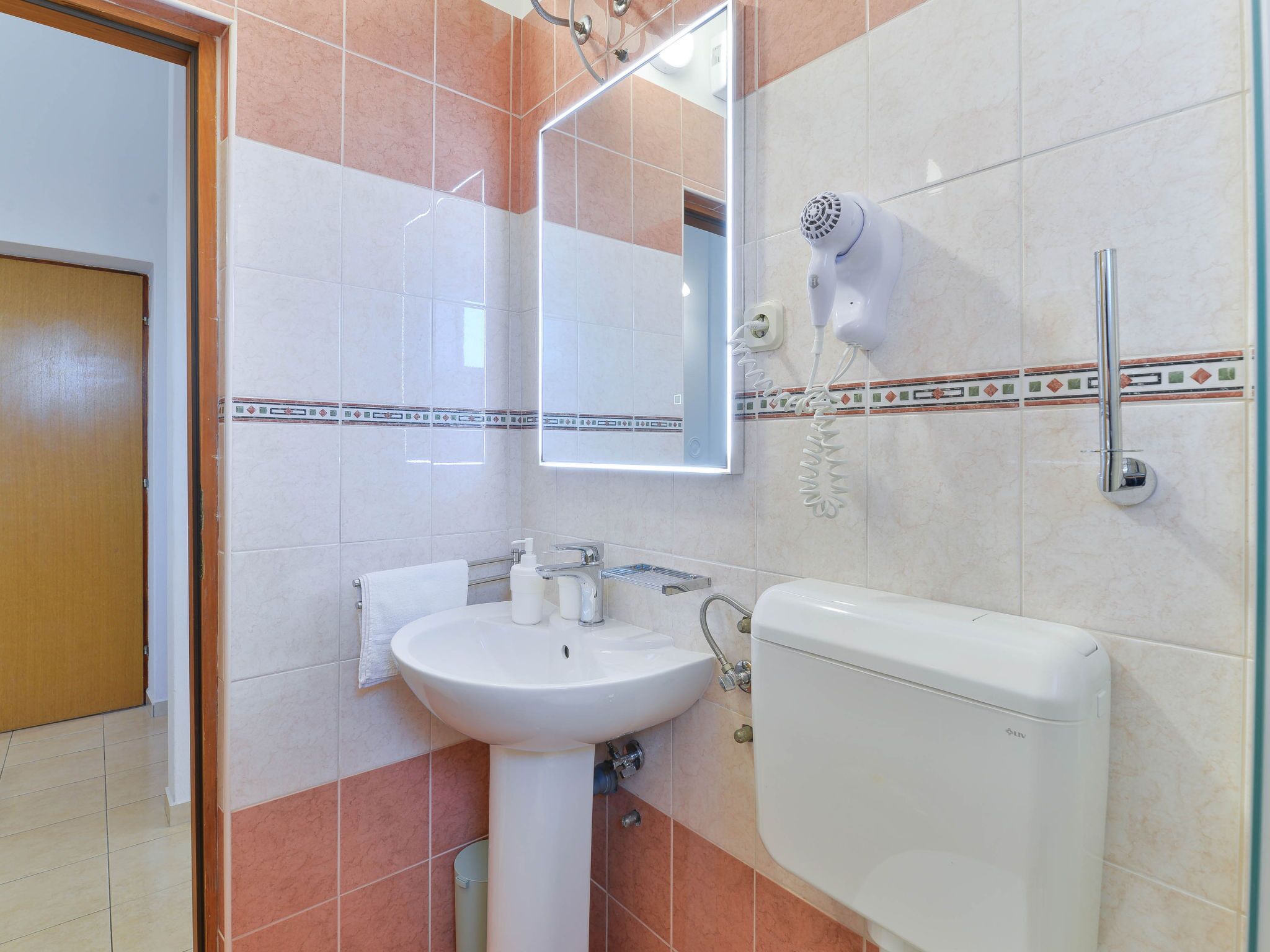Ein Badezimmer mit einem weißen Waschbecken, einem Spiegel, einem Handtuchhalter und einer Toilette.