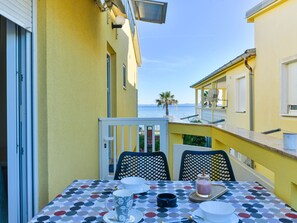 Ein Balkon mit Esstisch, mit Blick auf ein Gewässer und Gebäude.
