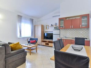 A compact living space with a sofa, a dining table, a TV, and a kitchenette. - Apartment  by Interhome (Vir)