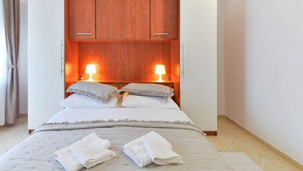 Un dormitorio con cama, dos lámparas de noche, un armario de madera y un par de toallas sobre la cama.
