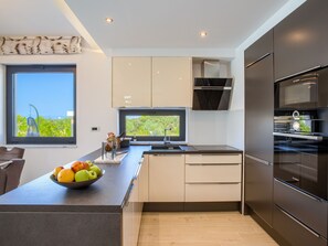 A modern kitchen with a large island, built-in appliances, and a view of greenery outside. - Beautiful villa Tamaria with heated pool by Interhome (Nin)