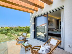 A balcony with two wooden chairs, a small table with a cup and saucer, and a glass door leading to a bedroom with a bed and a nightstand. - Beautiful villa Tamaria with heated pool by Interhome (Nin)